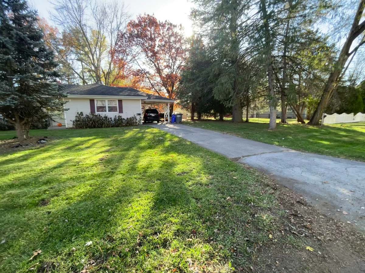 A freshly mown front lawn in autumn with a trimmed edge along a concrete driveway and a small brick house behind it.