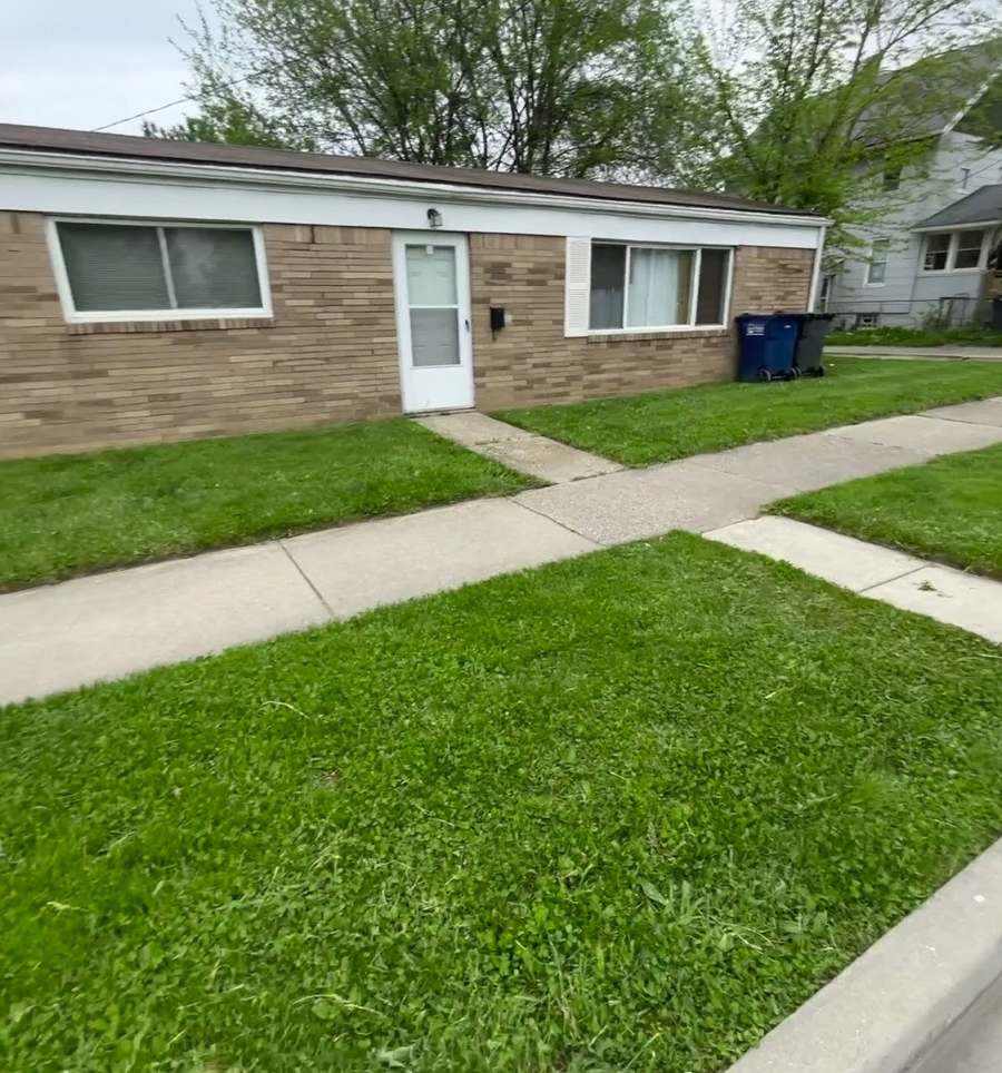 A low ranch house with a brick front, a neatly mown lawn and a concrete walk running past it to the curb.